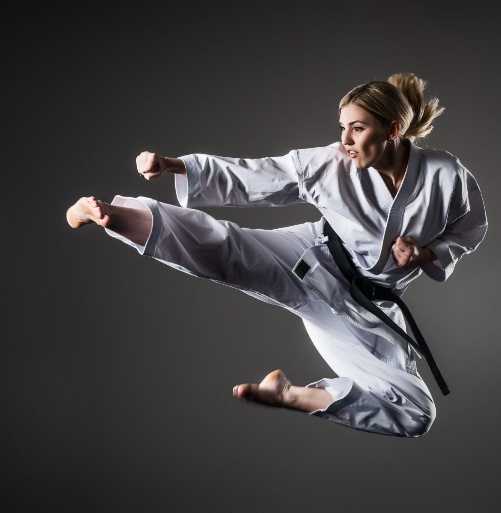 Composite image of karate girl in white kimono with black belt in jump. Purple background and clouds of smoke